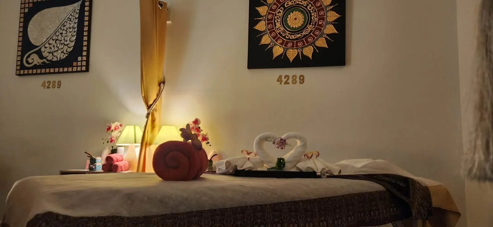 Candle-lit Thai massage treatment room with towel swans and traditional Thai art at Golden Orchid